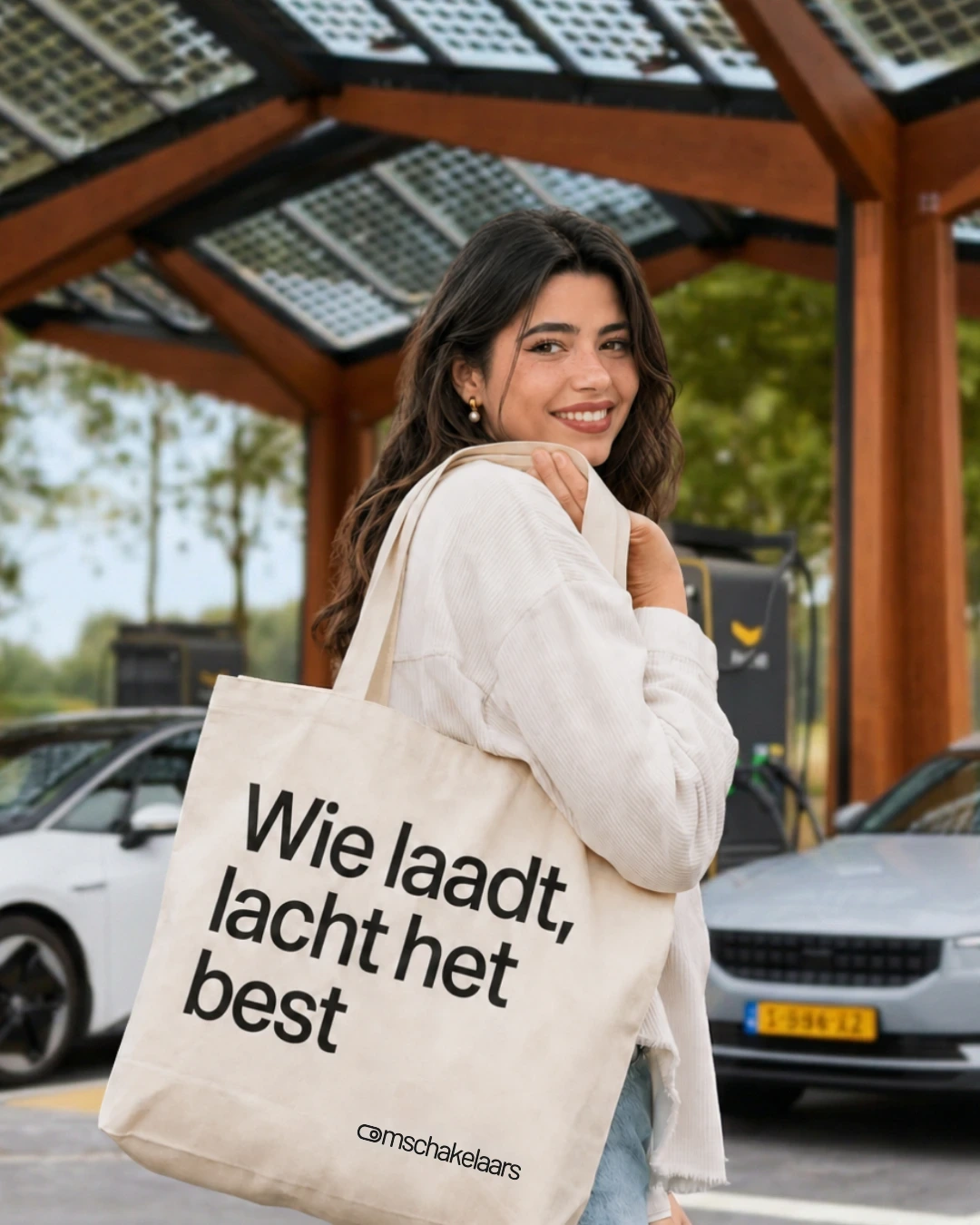 Lachende vrouw met een Omschakelaars-tas bij een laadplein met twee elektrische auto's